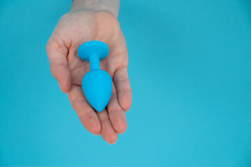 Woman holding a blue anal plug on a blue background. 