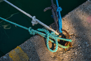 Mooring ring with tied blue and white nautical rope mounted on a concrete pier, marina safety...