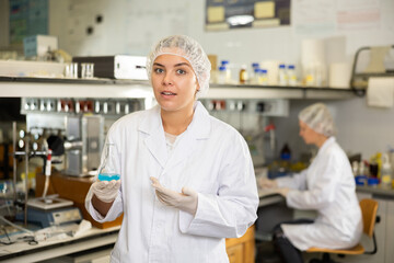 Portrait of young disturbed woman scientist working in research lab, holding flask with reagents
