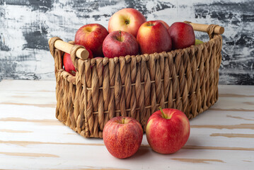 Ripe, juicy apples in a wicker basket on a white wooden table.