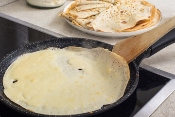 Delicious thin pancakes on a non-stick pan. cooking process.  A wooden spatula flips the pancake.