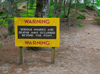 Sign on a  mountain trail warning hikers about dangerous area.