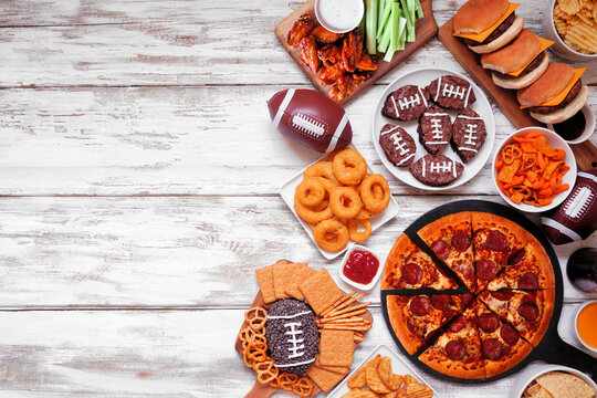 football food with pizza, burgers, wings. Overhead on white wood
