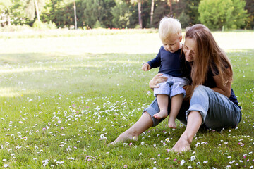 young mother with her son outdoor against beautiful summer field of daisy flowers