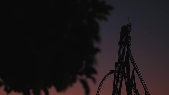 A night shot with a roller coaster on the background of a dark post-sunset sky. Roller coaster at night. An empty amusement park. The camera moves from left to right. High quality 4k footage