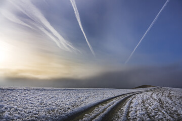Foggy winter landscape in hills and mountains with blue sky and plane tracks, hills with grass covered with snow, the road is summetric with plane tracks in the sky