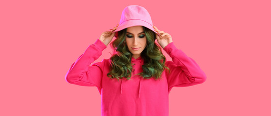 Beautiful young woman with unusual green hair on pink background