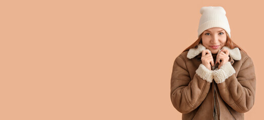 Young redhead woman in hat and warm sheepskin jacket on color background with space for text