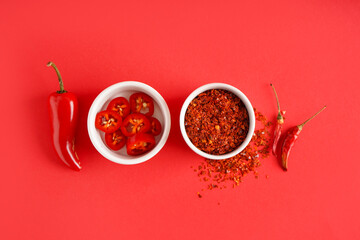 Bowls of chipotle chili flakes and fresh jalapeno pepper on red background
