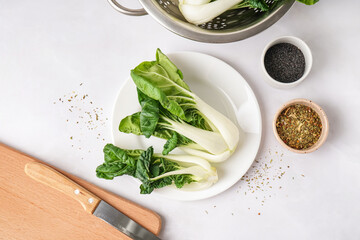 Plate with fresh pak choi cabbage and spices on light background