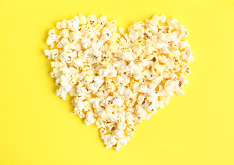 Heart made of tasty popcorn on yellow background