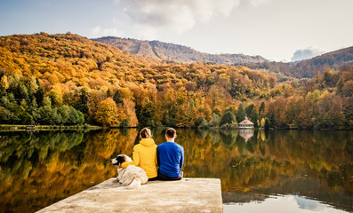 couple and dog sitting by beautiful autumn lake