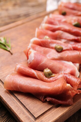 Wooden board with slices of delicious ham and capers, closeup