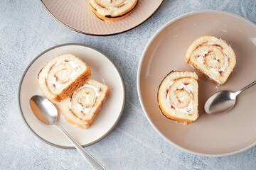Plates with pieces of delicious sponge cake roll and spoons on light table