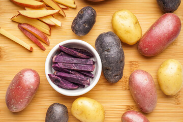 Wooden board with different raw potatoes, closeup