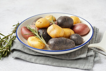Plate with different raw potatoes and rosemary on light background