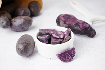 Bowl with slices of raw purple potato on light background