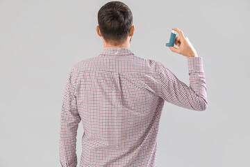 Man with inhaler on light background, back view
