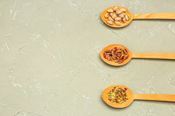 Spoons with unpeeled, peeled and sliced pistachio nuts on green background