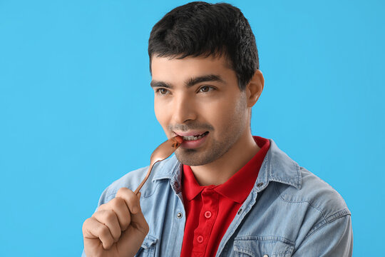 Young man with tablespoon on blue background, closeup