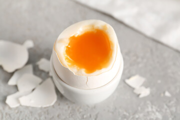 Holder with soft boiled egg and shell on grey table