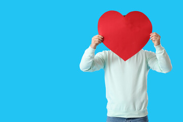 Young man with paper heart for Valentine's Day on blue background