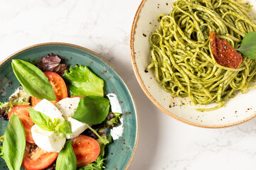 Top view of a plate of caprese salad next to a plate of pasta with pesto sauce. High quality photo