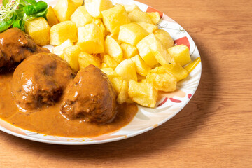 Plate of meatballs in sauce with french fries on wooden table. High quality photo