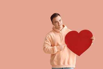 Young man with big paper heart for Valentine's Day on beige background