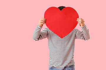 Young man with big paper heart for Valentine's Day on pink background