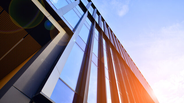 Glass modern building with blue sky background. Low angle view and architecture details. Urban abstract - windows of glass office building in  sunlight day.