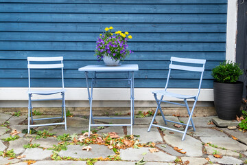 A purple colored metal patio table near a blue wooden horizontal clapboard siding exterior wall....