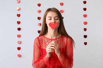 Young woman with paper heart for Valentine's Day on grey background