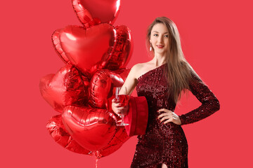 Young woman with glass of wine, gift and balloons on red background. Valentine's Day celebration