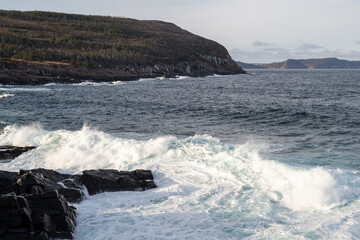 A seascape of a cloudy grey sky with a pink horizon that meets the grey ocean. There are a few...