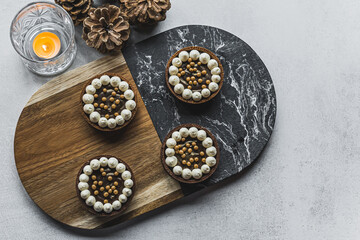 Obraz na płótnie Canvas Top view of four beautiful small chocolate tarts decorated with small meringues and pearls. Artistic bakery goods. High quality photo