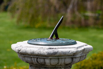 A brass sundial or shadow clock on a decorative concrete pedestal with a single metal angle rod celestial instrument. The sun dial measures the time on the mathematical clock using sunlight and shadow
