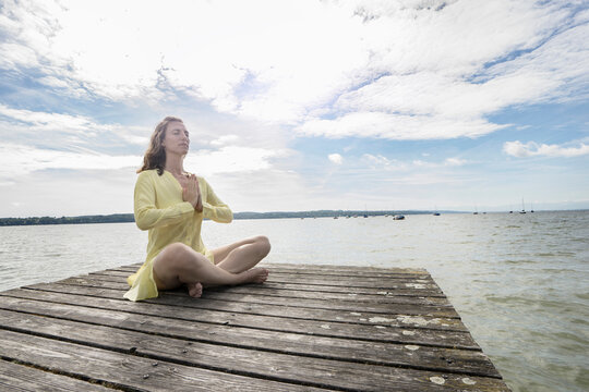 Woman doing lotus pose yoga on jetty at the lake, Ammersee, Upper Bavaria, Germany
