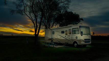 Rv camper parked under cloudy sunrise sky and trees at campsite 