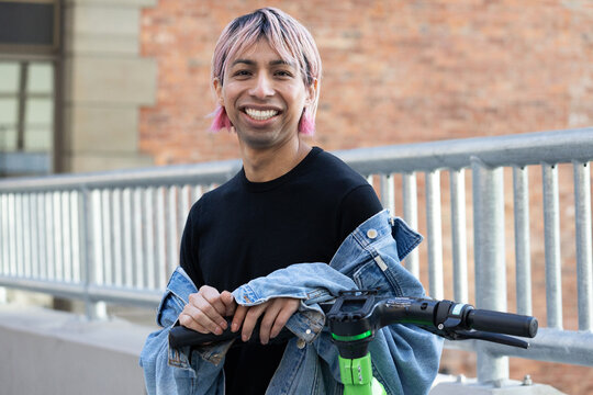 Non-binary person outside with an electric scooter.