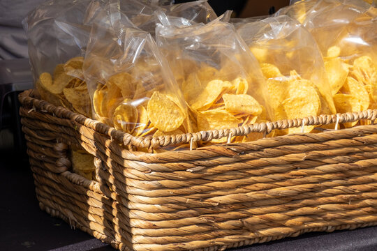 A Square Wicker Basket Filled With Small Clear Plastic Bags Of Round Yellow Organic Corn Chips. The Homemade Fried Mexican Tortilla Chips Are Packaged For Sale At A Market. The Crispy Chip Is Salty.