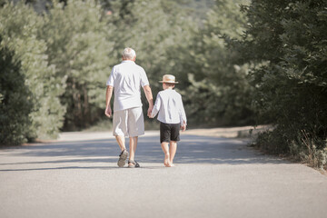 Back view of grandfather and grandson with hat walking on nature
