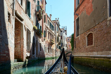 View from gondola with narrow canal of water surrounded by old buildings on sunny day in Venice, Italy. - obrazy, fototapety, plakaty