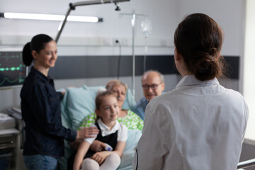 Obraz premium Nurse practitioner visiting happy elderly patient room in recovery. Sick grandmother smiling family chatting with unidentified female geriatric professional doctor at medical clinic room.