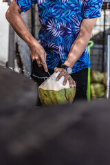 Frische grüne Kokosnuss wird von einem Mann am Strand aufgeschnitten um sie als Getränk zur...