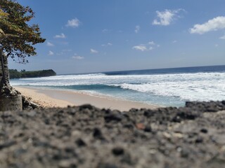 Weißer tropischer Sandstrand mit strahlend blauen Meer und einer Felsen im Hintergrund, Indonesien, Bali
