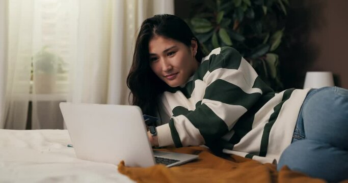Beautiful woman lying on bed in bedroom buys trip to exotic countries, uses online travel agency, bookable hotel, pays for vacation with credit card.