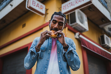 Portrait of a man biting a delicious burger because he is really hungry. He is outside in the city.