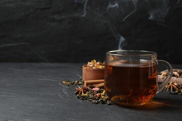 Glass cup of freshly brewed tea and dry leaves on black table. Space for text