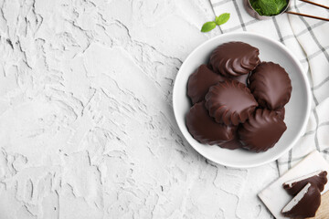Delicious chocolate covered zephyrs in bowl on light grey table, flat lay. Space for text
